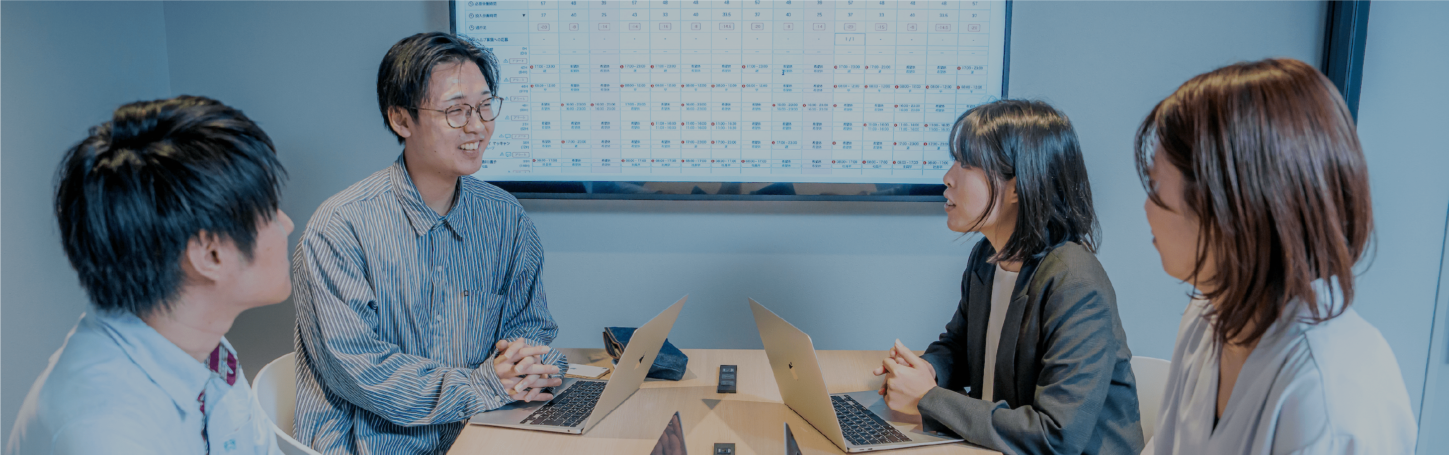 ノートパソコンを使いながら笑顔で会話する社員4人が集まる明るい室内の風景